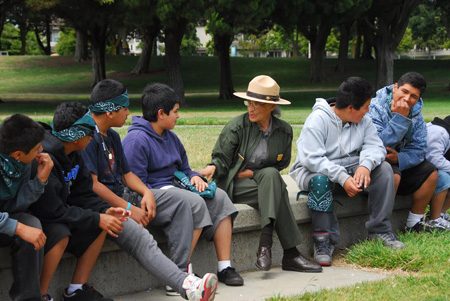 Betty Reid Soskin seated on a stone wall talking to a group of young boys visiting the park.